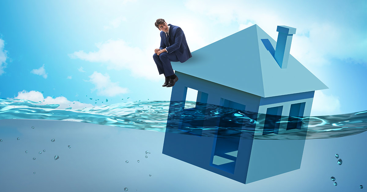 Ein Mann sitzt auf einem Haus, dass im Wasser schwimmt | Insolvenz Notverkauf Immobilie