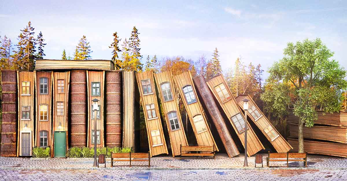 Holzhäuser in Buchform stehen aneinandergereiht vor einem Wald